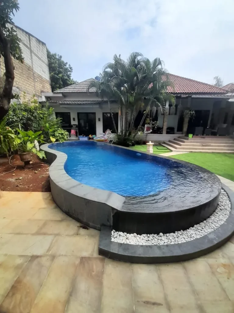 Kolam renang bentuk melengkung dengan tepi batu hitam dan taman rumput